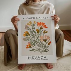 a woman sitting on the floor holding up a poster with flowers in it that reads flower market nevada