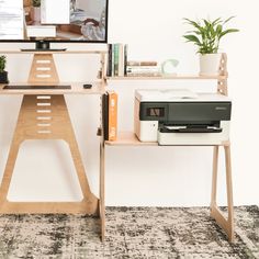 a computer desk with two computers on top of it next to a potted plant