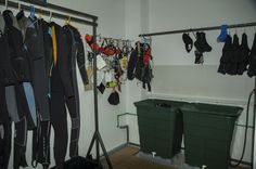 there are many coats hanging on the rack in this room with two bins and one green trash can