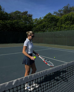 a woman holding a tennis racquet on top of a tennis court with a ball in her hand