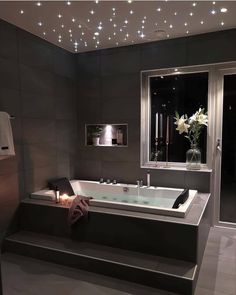 a bath tub sitting next to a window with lights on the ceiling and flowers in vase