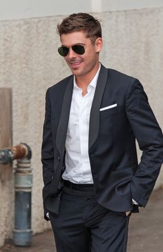 a man in a suit and sunglasses is standing on the street with his hands in his pockets