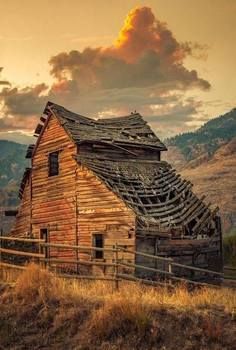 an old barn in the mountains with a wooden fence around it's sides and a cloudy sky above