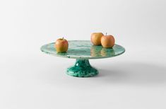 three apples sitting on top of a green cake plate in front of a white wall