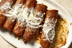 a white plate topped with meat covered in sauce and onions on top of breaded pastries