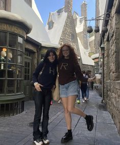 two women are walking down the street in front of hog potter's house at universal studios