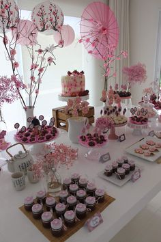 a table topped with lots of cupcakes and desserts covered in pink frosting