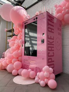 pink ice cream machine surrounded by balloons in an indoor space with white brick walls and flooring