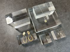 three clear acrylic boxes with gold jewelry on the floor next to each other