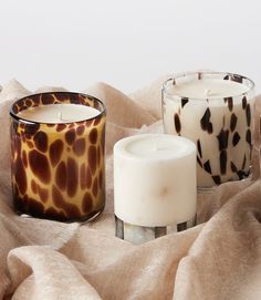 three candles sitting on top of a bed next to a brown and white animal print blanket