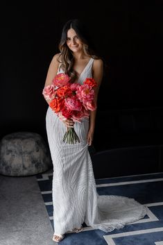 a woman in a white dress holding red and pink flowers while standing on a rug