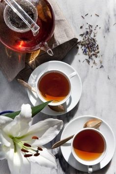 two cups of tea sit next to each other on a marble table top with spoons