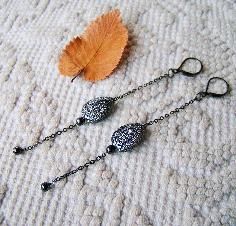 two long chain earrings with black beads and a leaf laying on the ground next to it