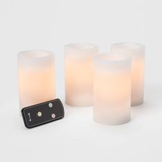 four lit candles and a remote control on a white surface