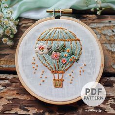 an embroidery pattern with flowers and a hot air balloon in the middle on a wooden surface