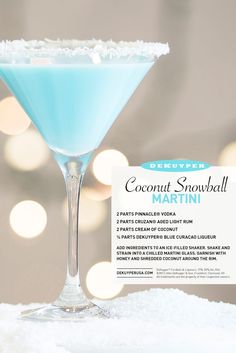 a blue cocktail in a martini glass sitting on top of snow