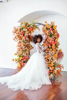 a woman standing in front of a floral arch with orange and yellow flowers on it