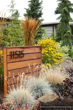 a wooden sign sitting in the middle of a garden filled with lots of plants and flowers