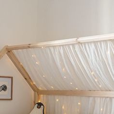 a bed with white sheets and string lights on the headboard is under a canopy