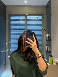 a woman taking a selfie in front of a bathroom mirror with her cell phone