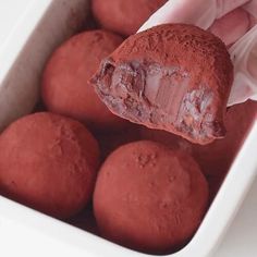 a hand holding a chocolate truffle in a white dish with other food items