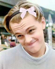 a woman with a pink bow in her hair smiles at the camera while wearing a gray sweater