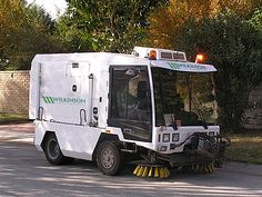 a street sweeper is parked on the side of the road in front of some trees