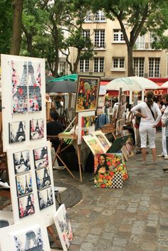 an outdoor market with people looking at art on display