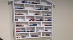 a white book shelf filled with toy cars on top of a wooden floor next to a wall