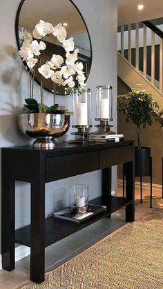 a black console table with white flowers and candles on it in front of a staircase