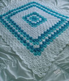 a crocheted blanket on a bed with white sheets and blue trimmings