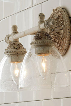 two clear glass globe lights are hanging from the side of a white wall mounted light fixture