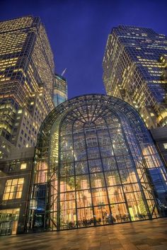 two large glass buildings in the middle of a city at night with lights shining on them