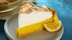 a slice of lemon meringue pie on a white plate with a blue tablecloth