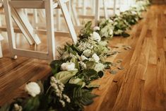 the aisle is lined with white flowers and greenery