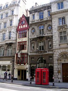 two red phone booths are in front of an old building on the corner of a street