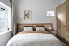 a bed with white sheets and pillows in a bedroom next to a large wooden cabinet