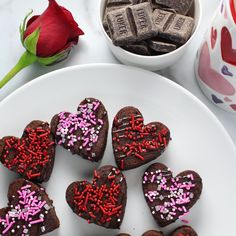 heart shaped brownies with sprinkles on a plate next to a rose