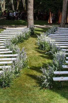 rows of white wooden benches sitting next to each other on top of a lush green field