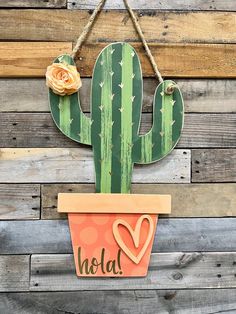 a cactus shaped sign hanging on the side of a wooden wall next to a flower pot