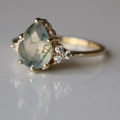 a gold ring with an aqua green stone and three diamonds on the side, sitting on a white surface