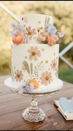 a white cake with flowers on it sitting on top of a wooden table next to napkins