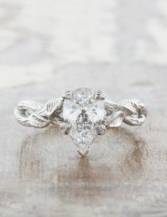 a white gold engagement ring with an oval cut diamond in the center and leaves on each side