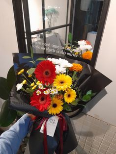 a person holding a bouquet of flowers in front of a mirror with a sign on it