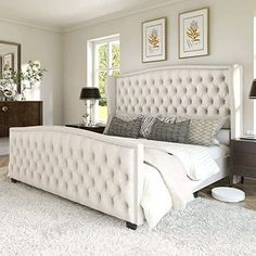 a large white bed sitting in a bedroom next to a dresser and two lamps on either side of the bed