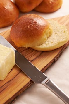 bread and butter are on a cutting board with a knife next to the buns