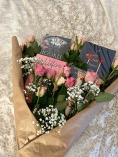 a bouquet of roses and books in a wrapper on top of a white bed