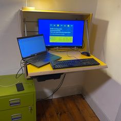 two laptop computers sitting on top of a yellow desk next to a green file cabinet