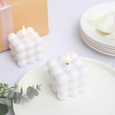 a white plate topped with two candles next to a box and some plates on the table