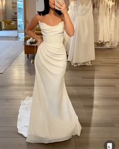 a woman in a white dress taking a selfie with her cell phone while wearing a wedding gown